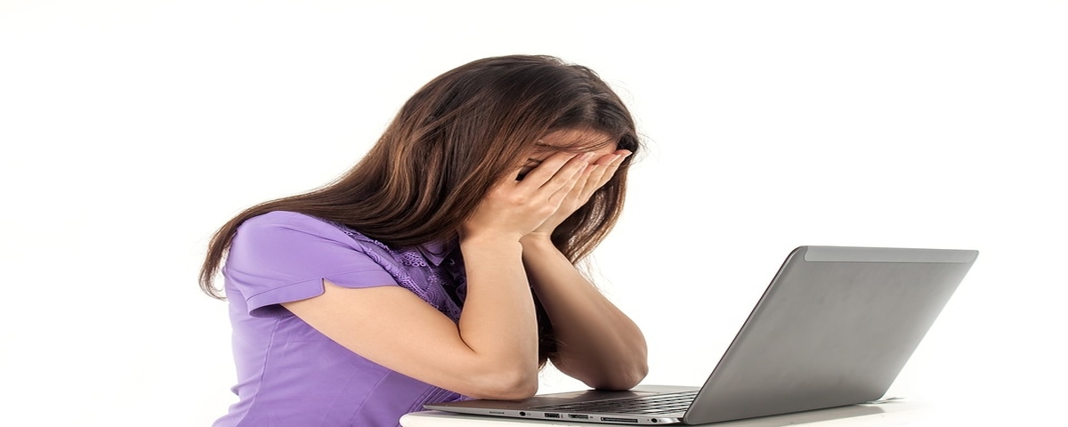 Female in distress with hands over her face while she browses social media on her laptop computer.