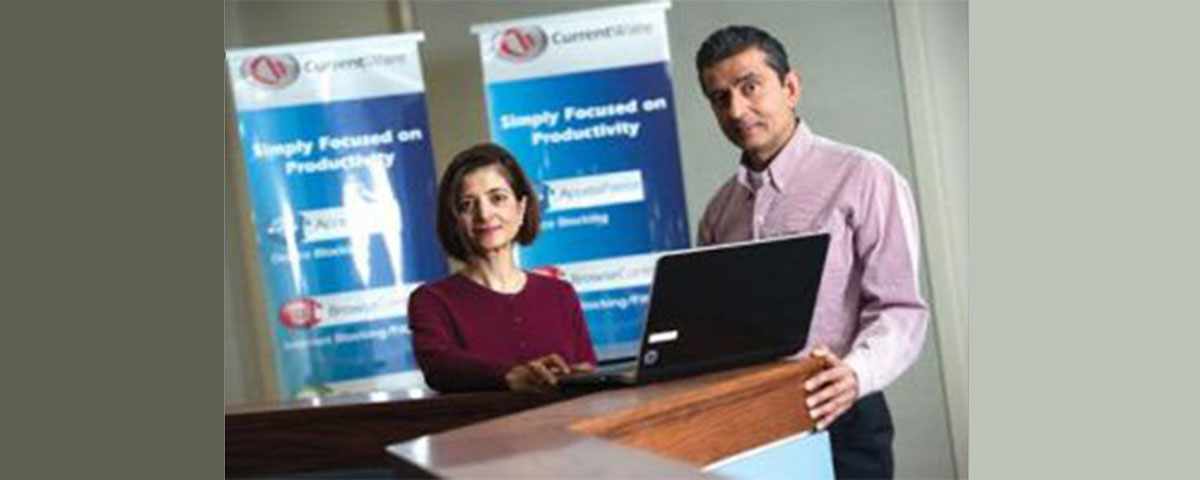 Sue and Jay from CurrentWare standing in front of the CurrentWare banners with a laptop computer.