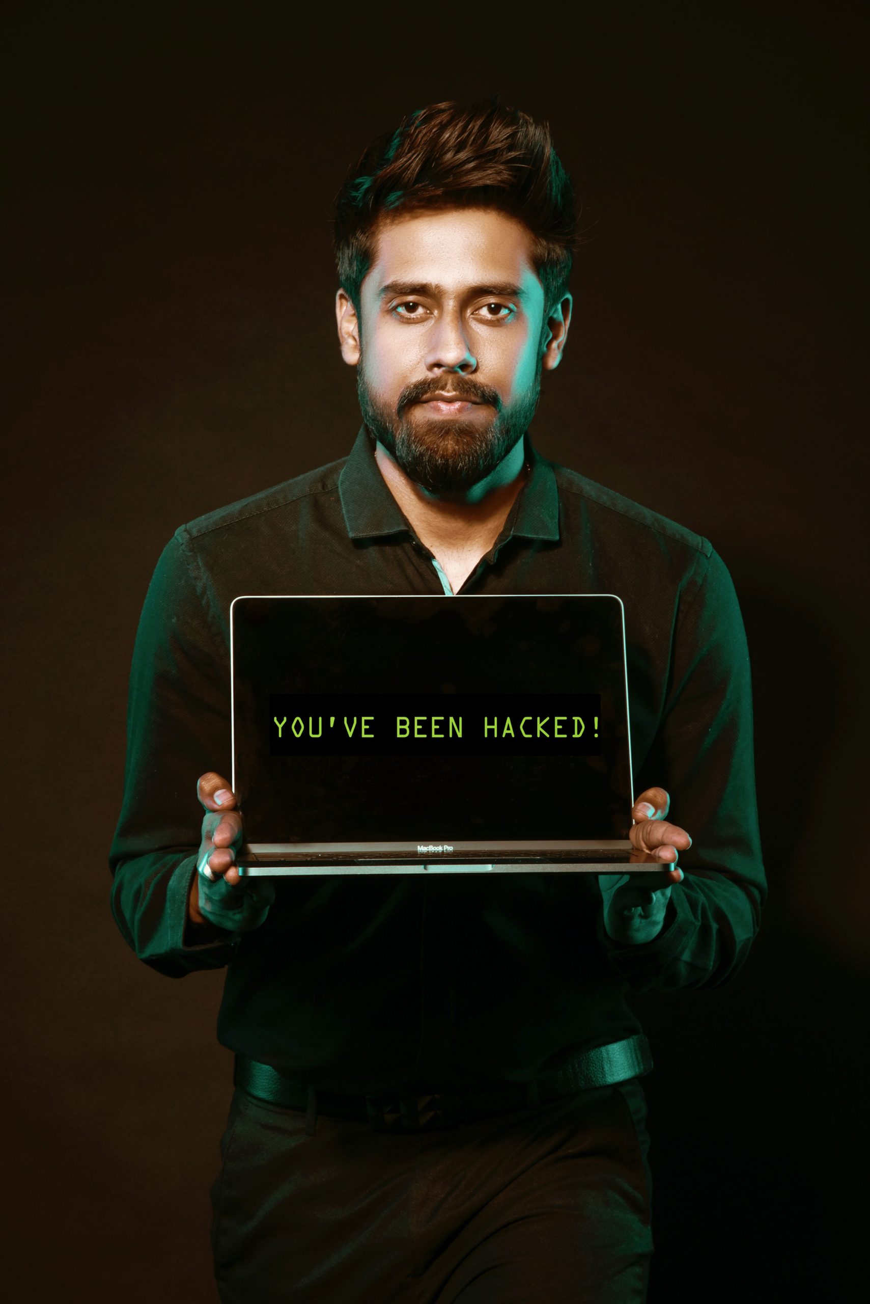 Man holding up a laptop computer. The computer says "you've been hacked"