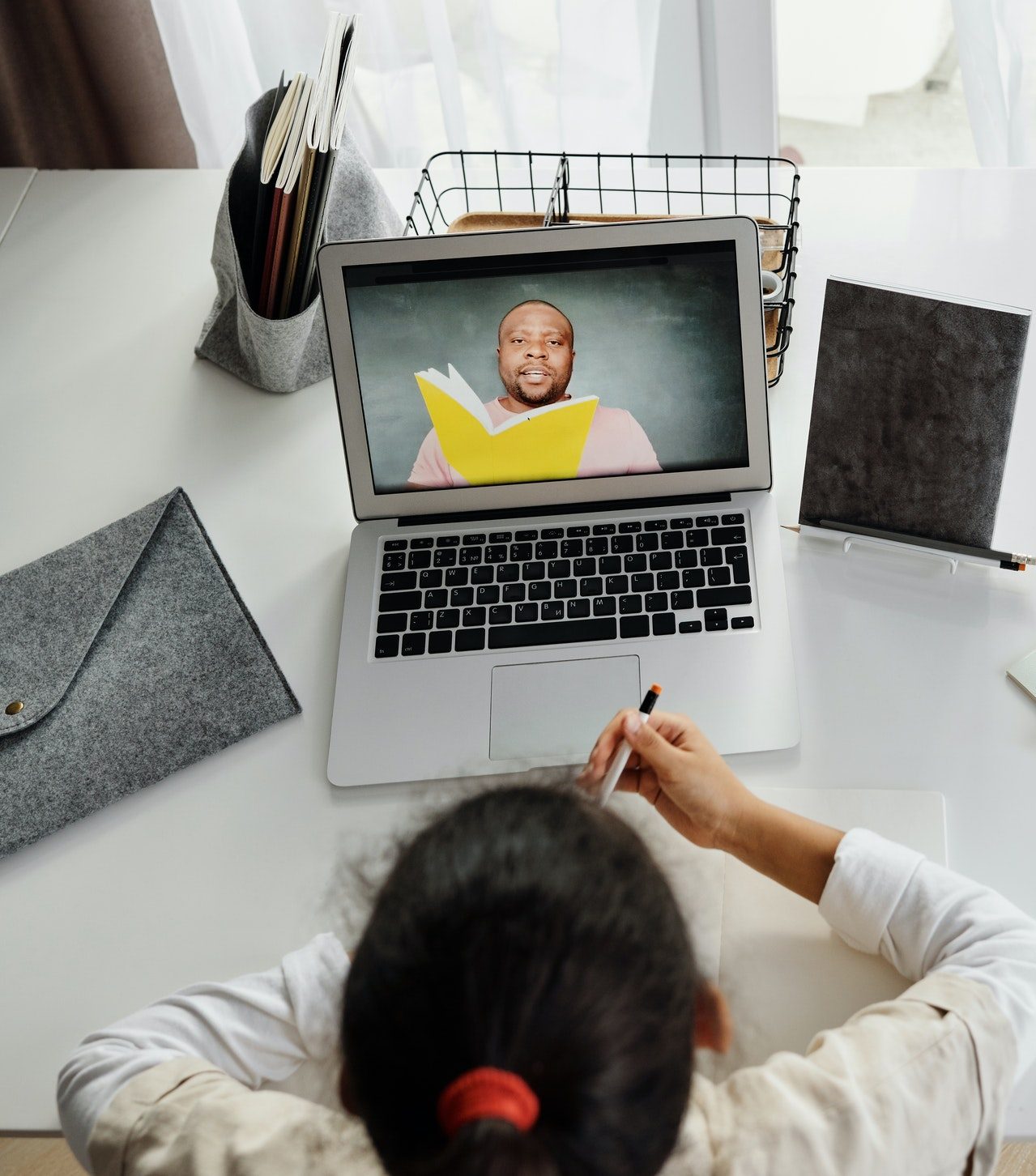 A young girl watches her teacher provide a lesson through her laptop. She is in her own home.