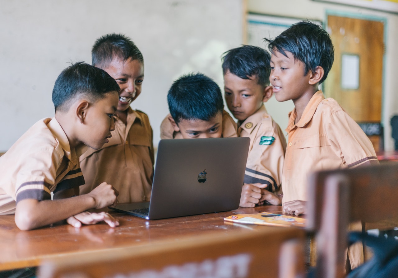 A group of young boys surround a laptop computer. We cannot see what is on-screen but they are clearly amused.