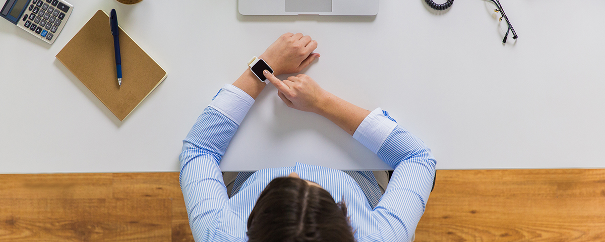A professional manages his time by looking at his watch. He is sitting at his desk.
