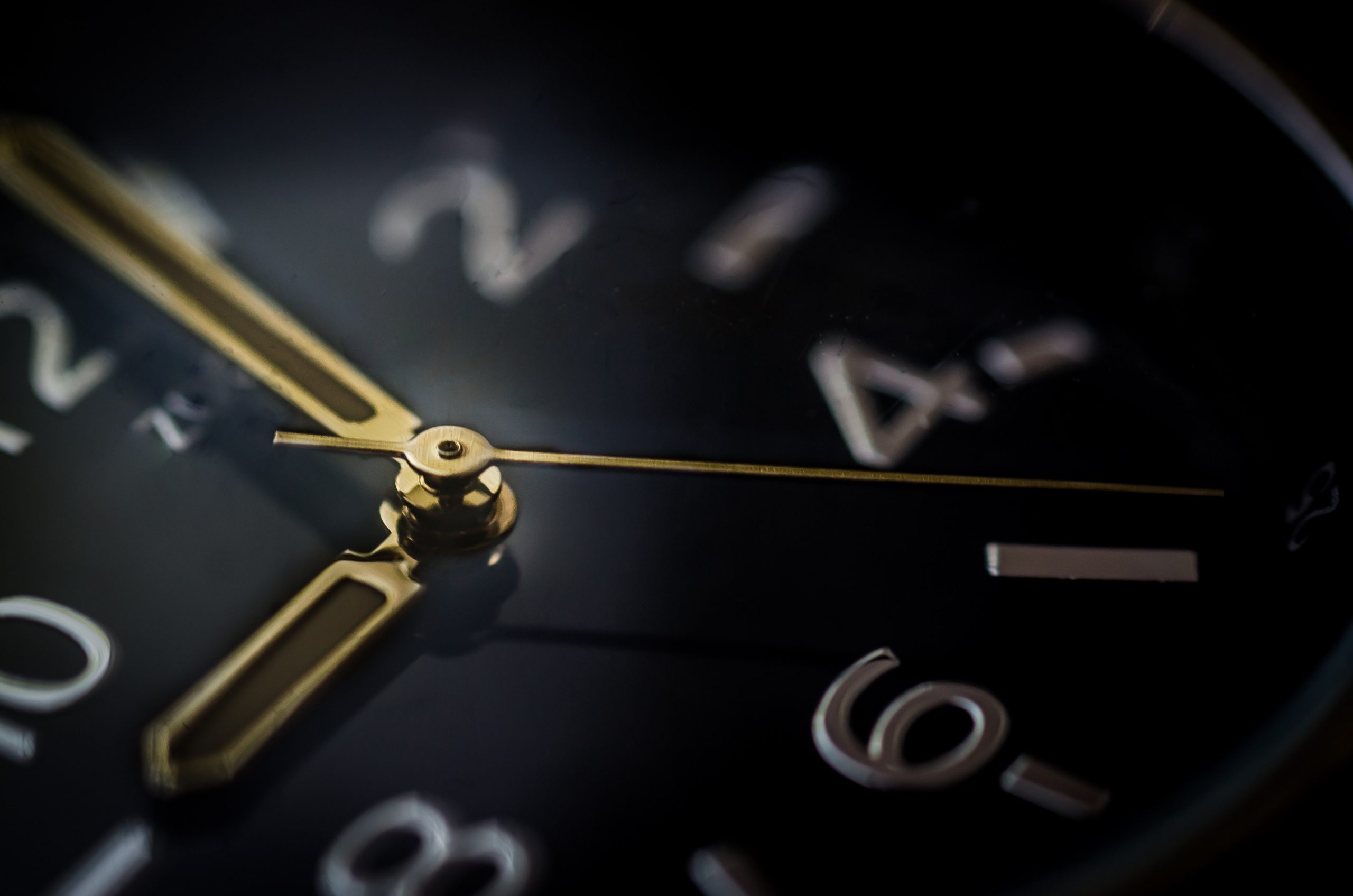 a closeup picture of a clock. It has a black face, silver numbers, and gold hands