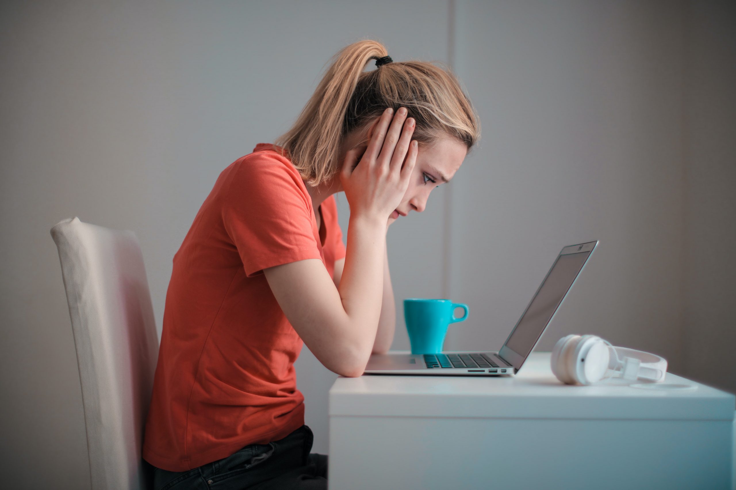 A stressed woman stares are her laptop screen. Her face is held in her hands.