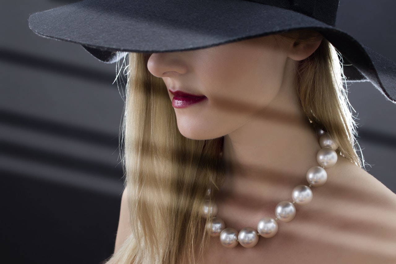 Woman hiding her eyes with a wide-brimmed hat. Luxury look with red lipstick and large pearl necklace