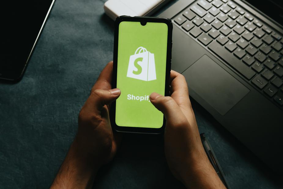 Hands holding a cell phone showing the shopify logo