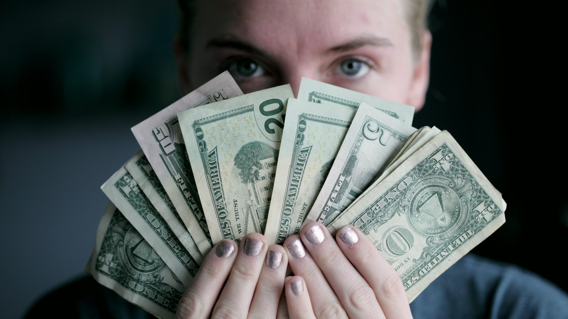 A woman holds various denominations of united states dollars in front of her face